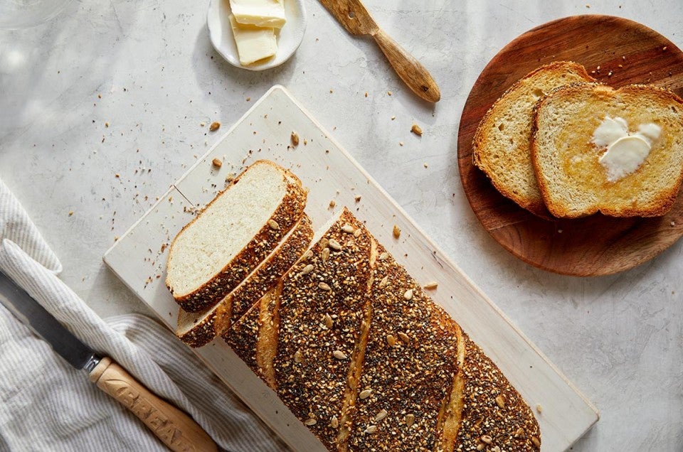 A loaf of chewy semolina rye bread cut into slices with a few pieces toasted on a plate