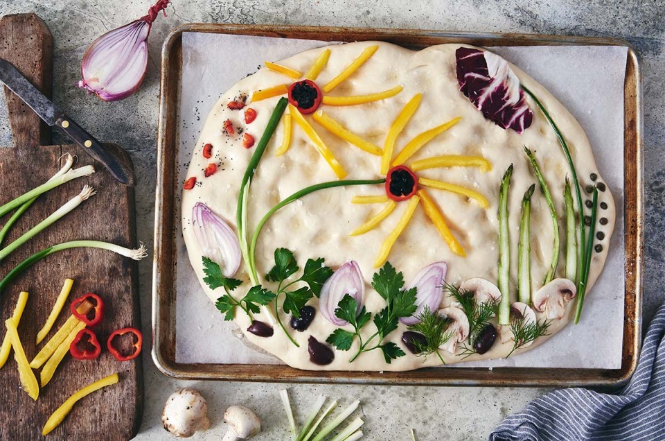 Focaccia dough topped with vegetables arranged in a garden scene