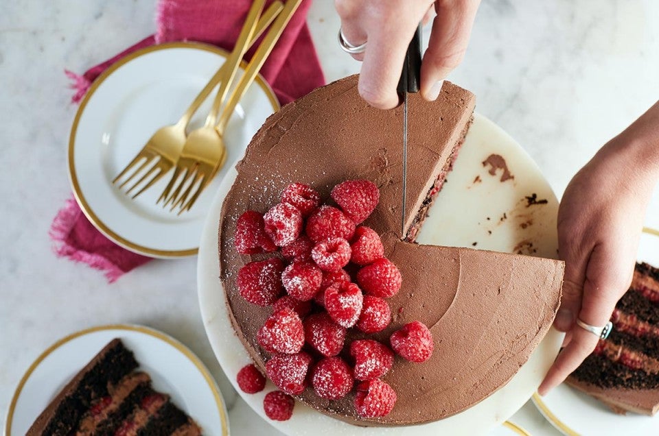 A chocolate mousse cake with raspberries being sliced