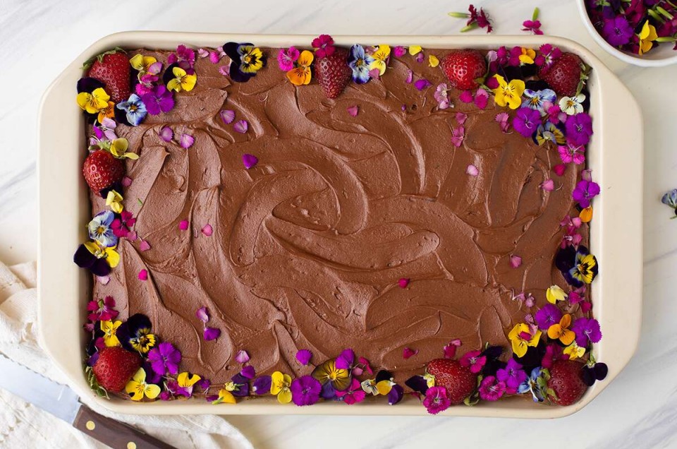 A sheet cake topped with chocolate frosting and edible flowers