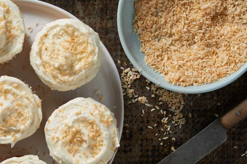 Bowl of toasted coconut next to cupcakes