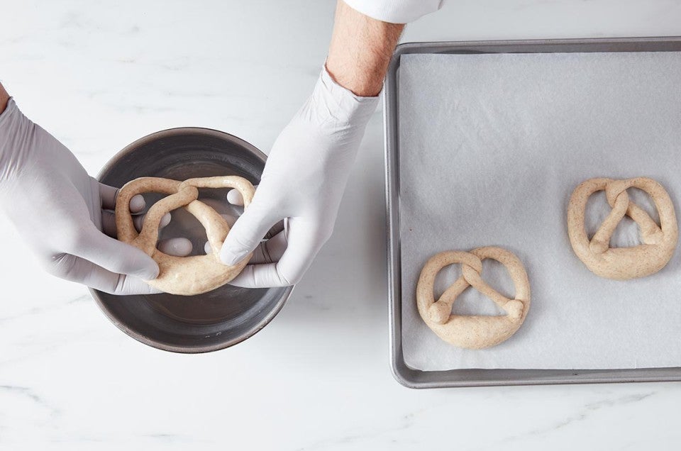 Hands dipping pretzels with lye