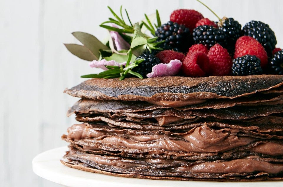 A chocolate cake made from stacked crepes and filled with pastry cream, topped with berries