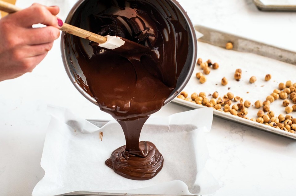 A baker pouring melted chocolate onto a sheet pan to make chocolate bark