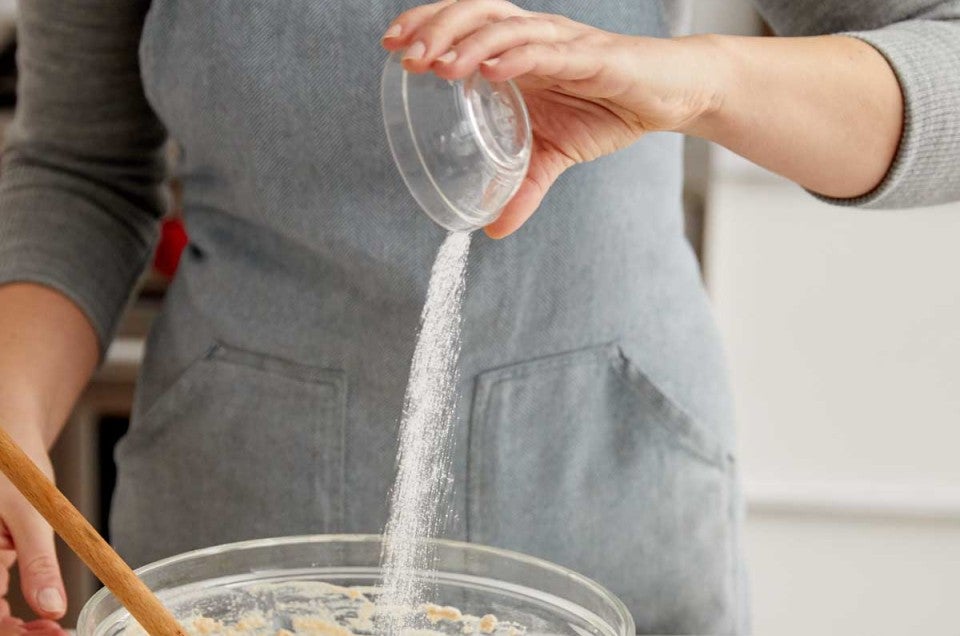 Hand pouring salt into bowl of dough