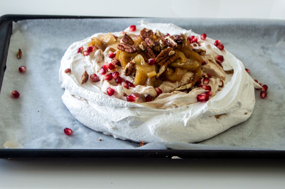 Winter pavlova topped with pomegranate seeds, baked apples, and nuts