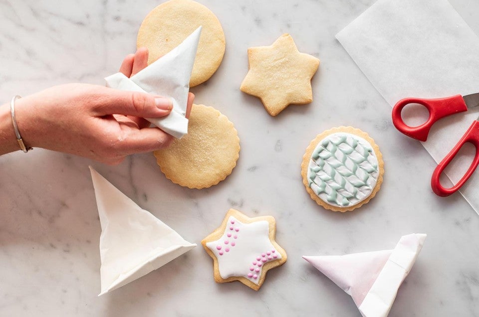 Cornet being used to decorate cookies with pink dots and green stripes