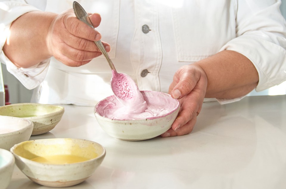 Hands mixing frosting with natural pink coloring