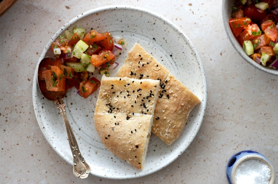 Two slices of Afghan Naan on a plate next to a tomato salad - select to zoom