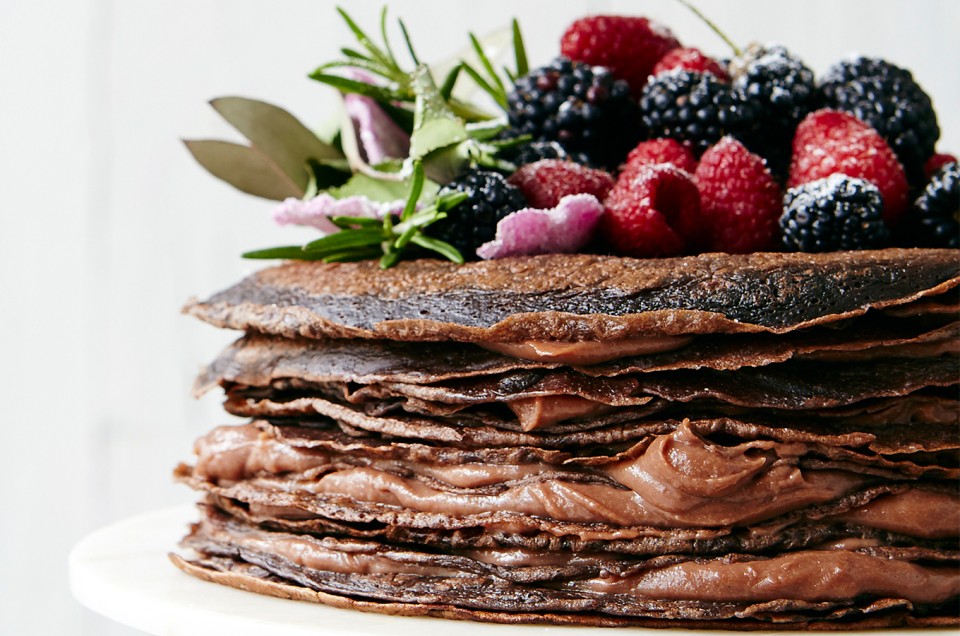 A chocolate cake made from stacked crepes and filled with pastry cream, topped with berries