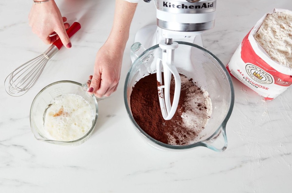 Ingredients for chocolate cake being added to a stand mixer bowl