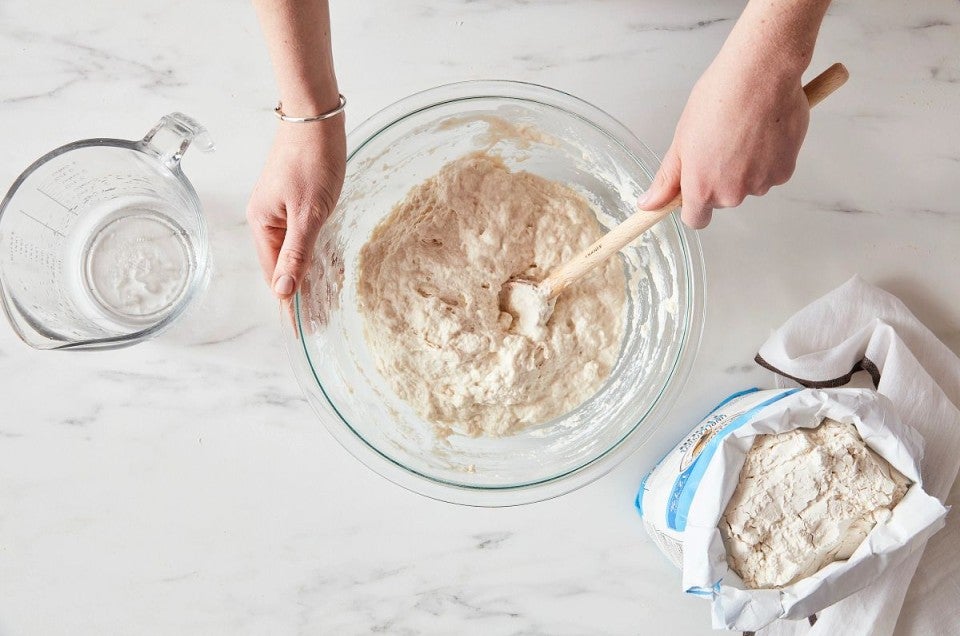 Baker mixing bread dough next to open bag of bread flour