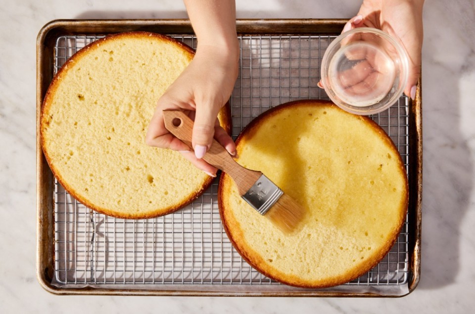 Baker brushing simple syrup cake soak onto round cake layer