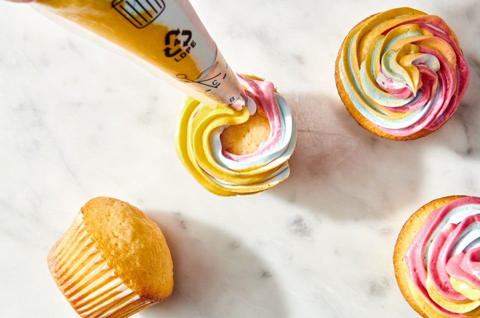 Rainbow frosting being piped on cupcakes