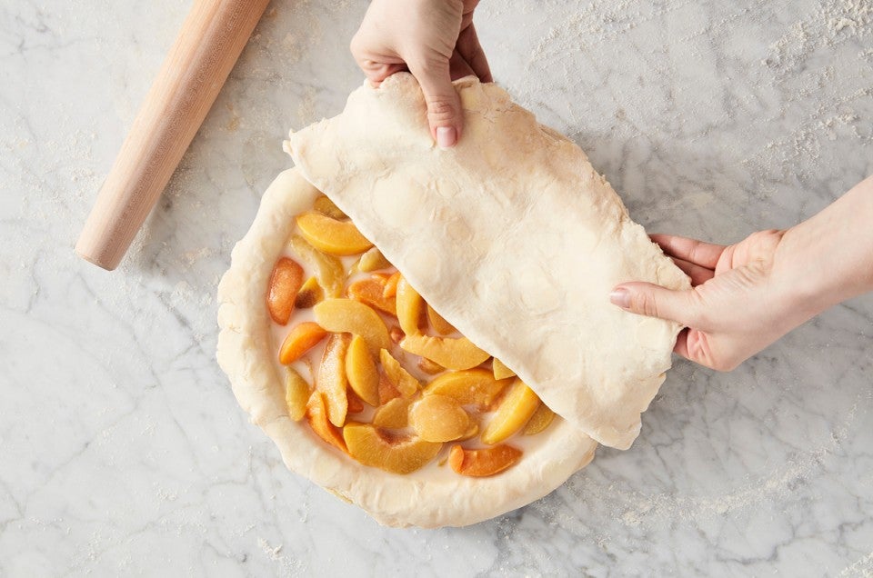 Baker putting top pie crust over filling in pie pan