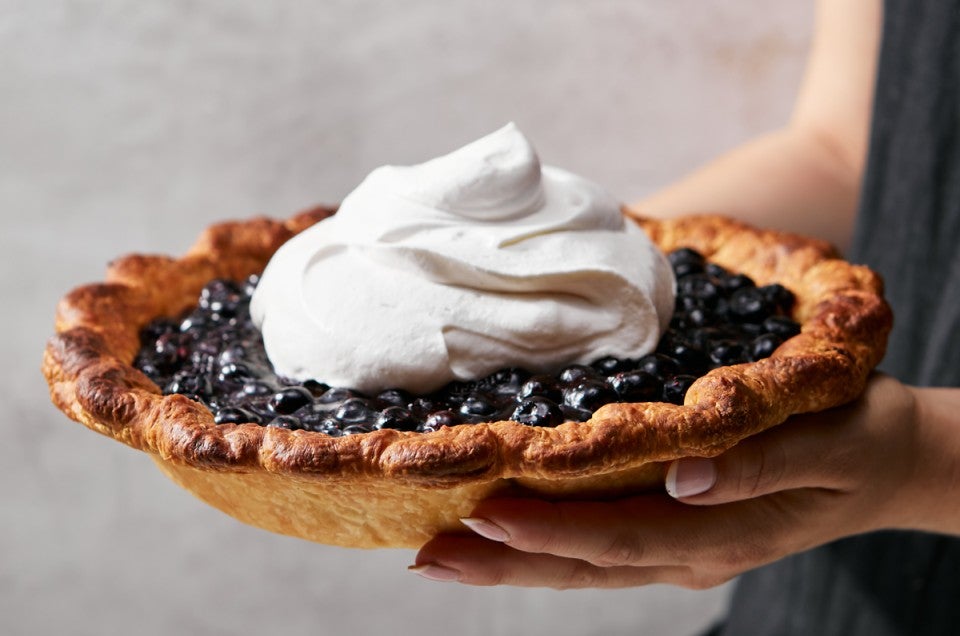 Baker holding whole blueberry pie outside of its pan