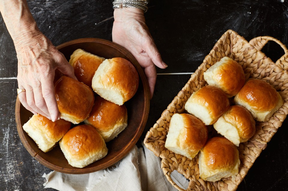 A baker putting soft white dinner rolls into a bread basket