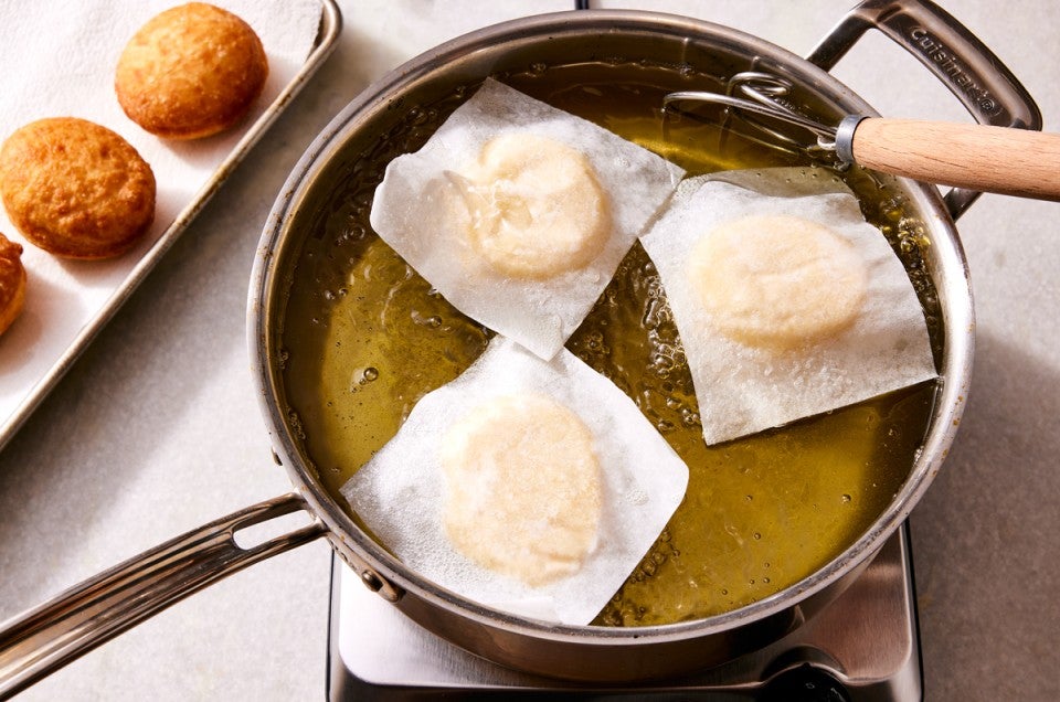 Doughnuts being fried on squares of parchment paper