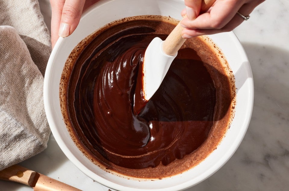 Baker using spatula to stir a bowl of ganache