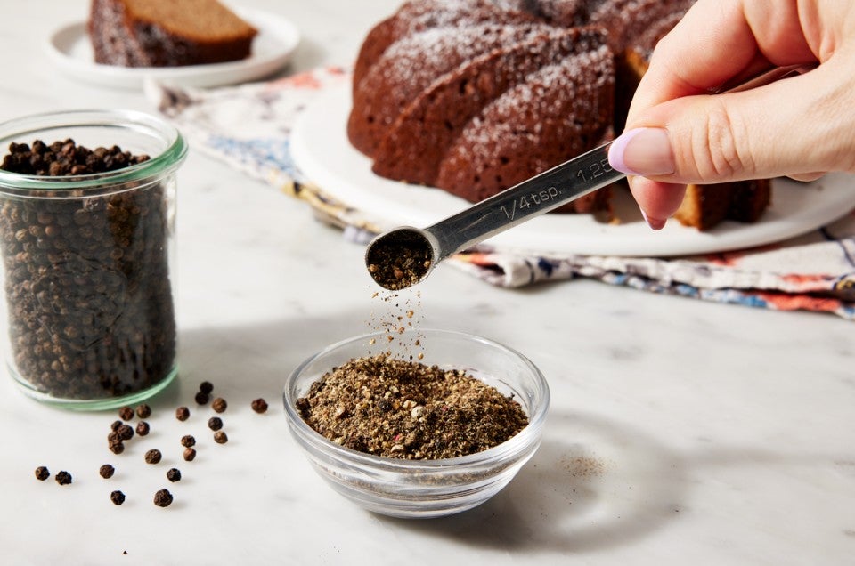 Small glass bowl of ground pepper in front of a Bundt cake