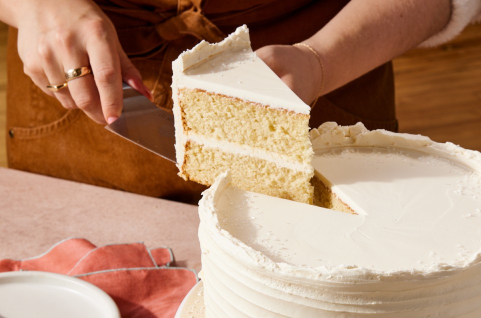 Baker cutting a slice of white velvet cake