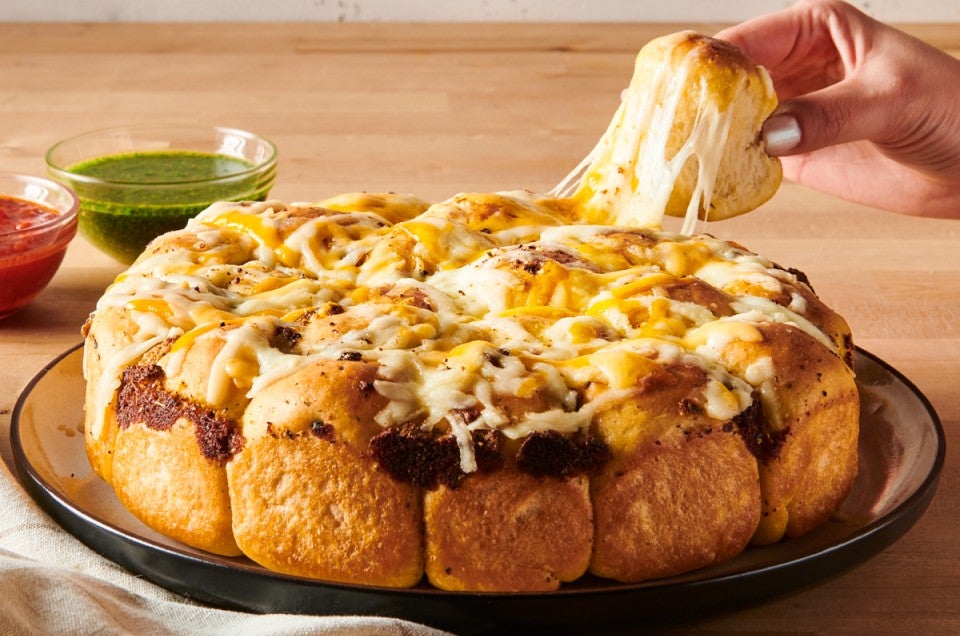 Hand pulling a cheesy roll from a batch of pull apart rolls