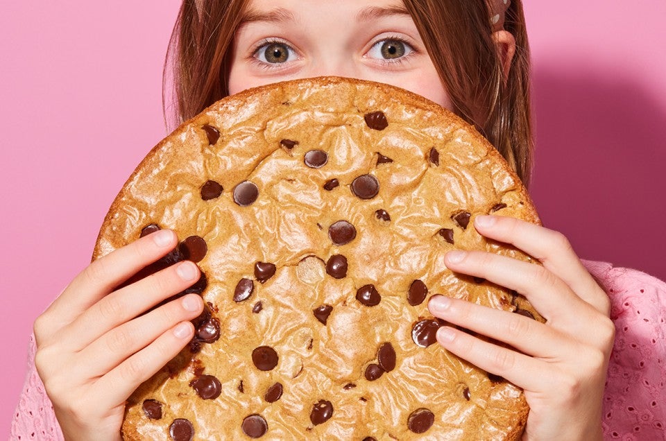 A young girl hiding behind a Chocolate Chip Skillet Cookie - select to zoom