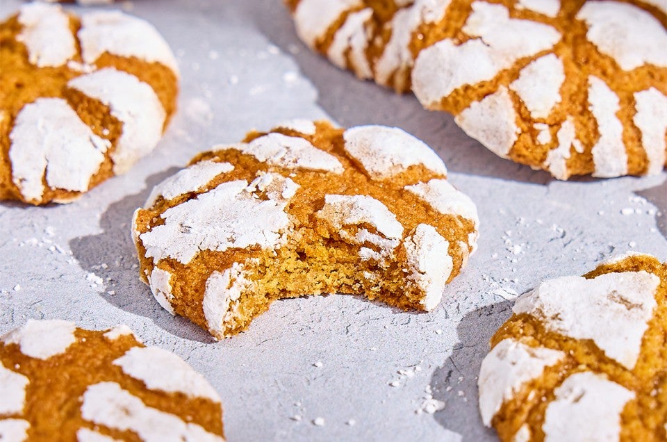 Pumpkin Crinkle Cookies on parchment paper; one with a bite taken - select to zoom