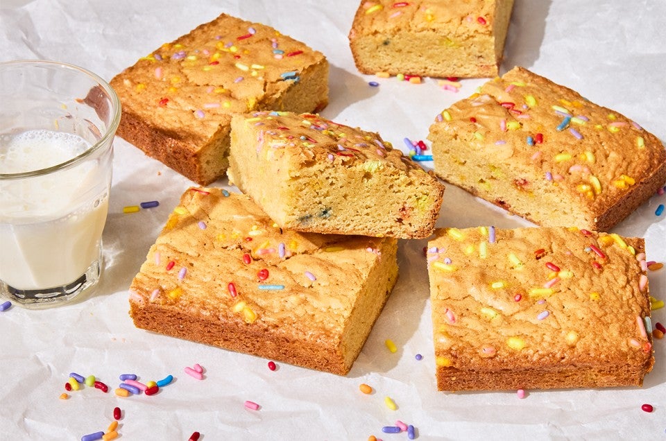 Small-Batch Birthday Cake Blondies on a counter with a glass of milk - select to zoom