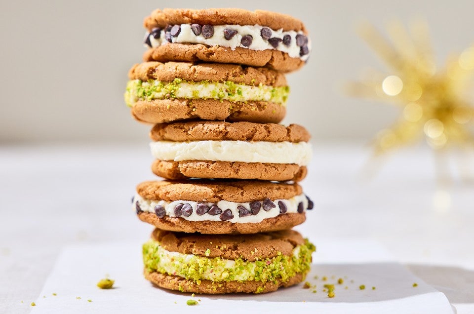 Stacked cannoli sandwich cookies showing the cookies, a layer of filling, and chocolate chips or pistachio coating. - select to zoom