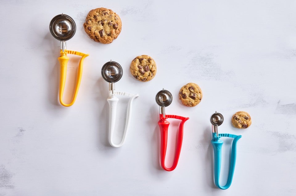 Different sizes of kitchen scoops next to chocolate chip cookies