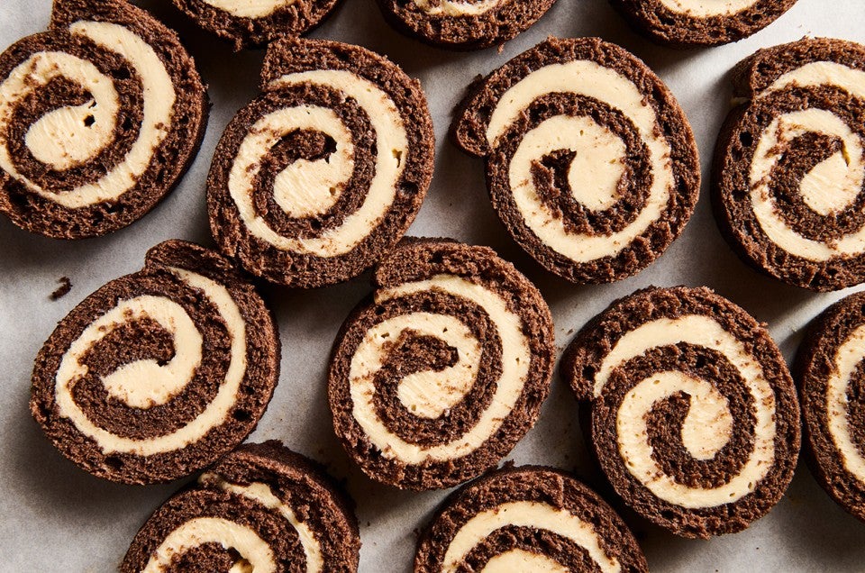 Sliced pinwheels of chocolate cake filled with Cookie Butter Whipped Ganache all laying side by side on a sheet tray. - select to zoom