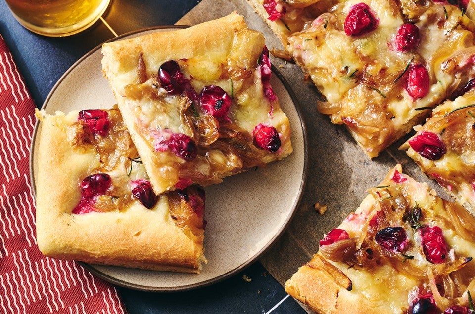 Slices of Caramelized Onion and Brie Pizza on a plate showing a golden baked top dotted with pomegranate, brie, and caramelized onion. - select to zoom