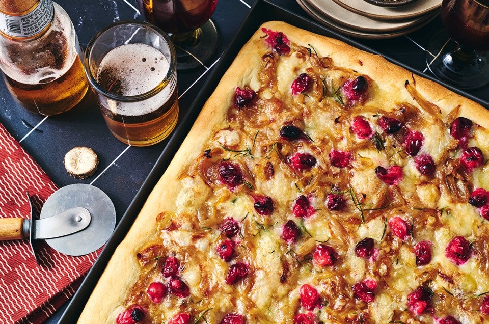 Caramelized Onion and Brie Pizza fresh out of the oven showing a golden baked top dotted with pomegranate, brie, and caramelized onion. - select to zoom