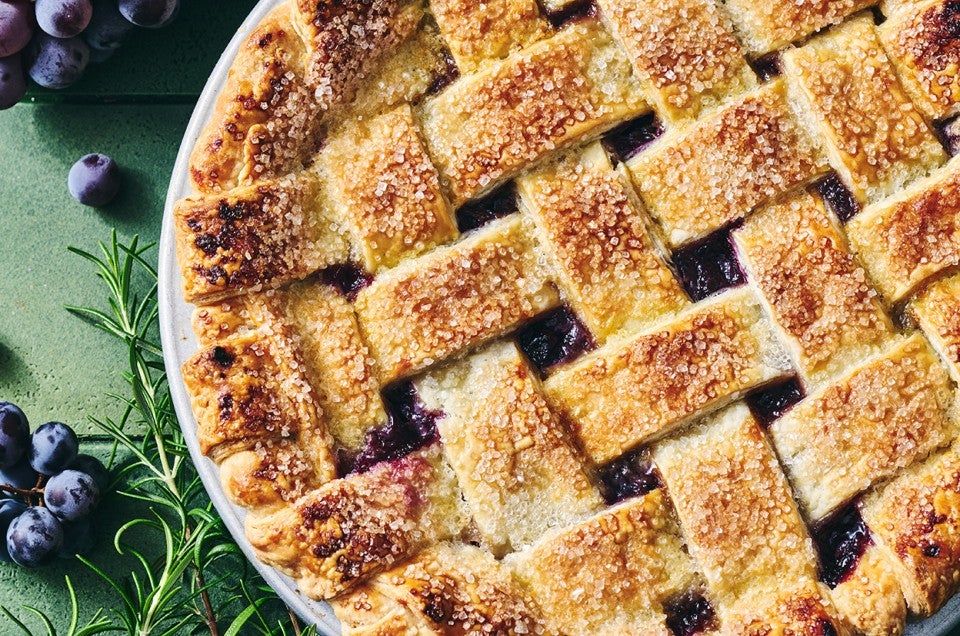 Concord Grape Pie photographed from above showing a lovely woven pie crust on top with brown hues and coarse sugar. - select to zoom