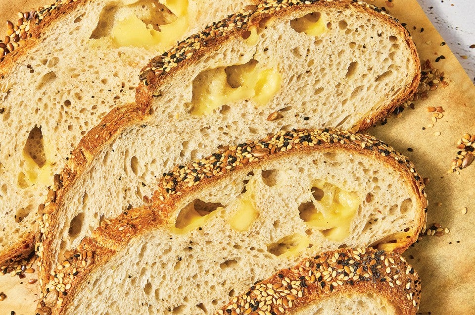 Detail of Parmesan Black Pepper Sourdough Bread sliced and laid out on a wooden cutting board showing an airy bread with cheese in the air pockets. - select to zoom