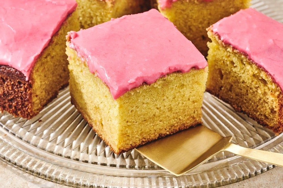 Slices of Cranberry-Orange Olive Oil Cake on a glass plate with golden cake and a pastel pink frosting. - select to zoom