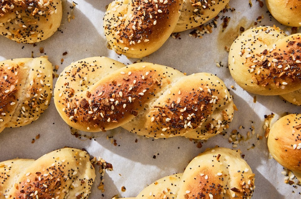 A close up of an Everything Bagel Twist shown fresh out of the oven on parchment with a lovely brown top and bits of everything bagel seasoning. - select to zoom