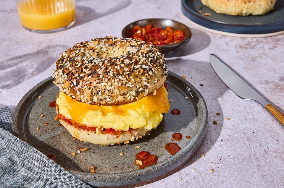 A breakfast sandwich with egg and cheese between a delicious everything bagel on a plate. - select to zoom