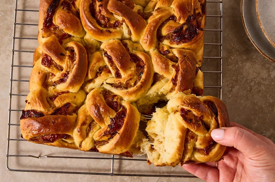 A hand pulling a French Onion Roll from the bake fresh out of the oven. - select to zoom