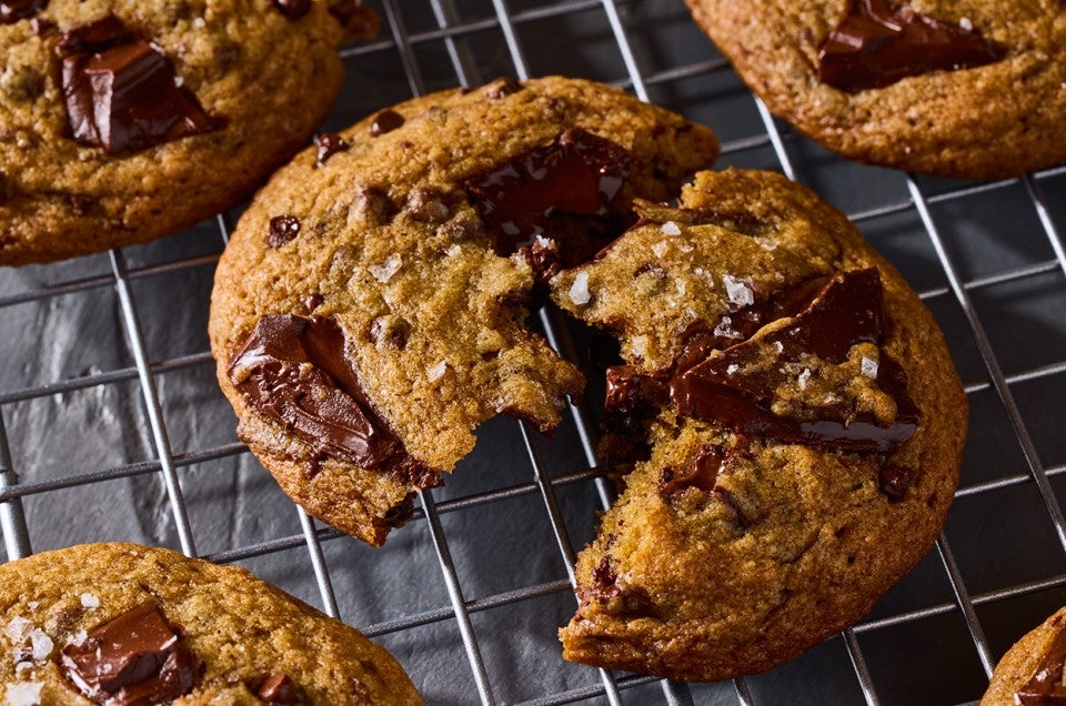 A High-Altitude Chocolate Chip Cookie split on a cooling rack showing the brown color of the dough and the gooey large chocolate bits in the cookie. - select to zoom