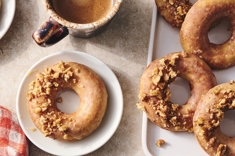 A Maple Donut on a plate with half coated in broke nut meat and the other half glazed. - select to zoom