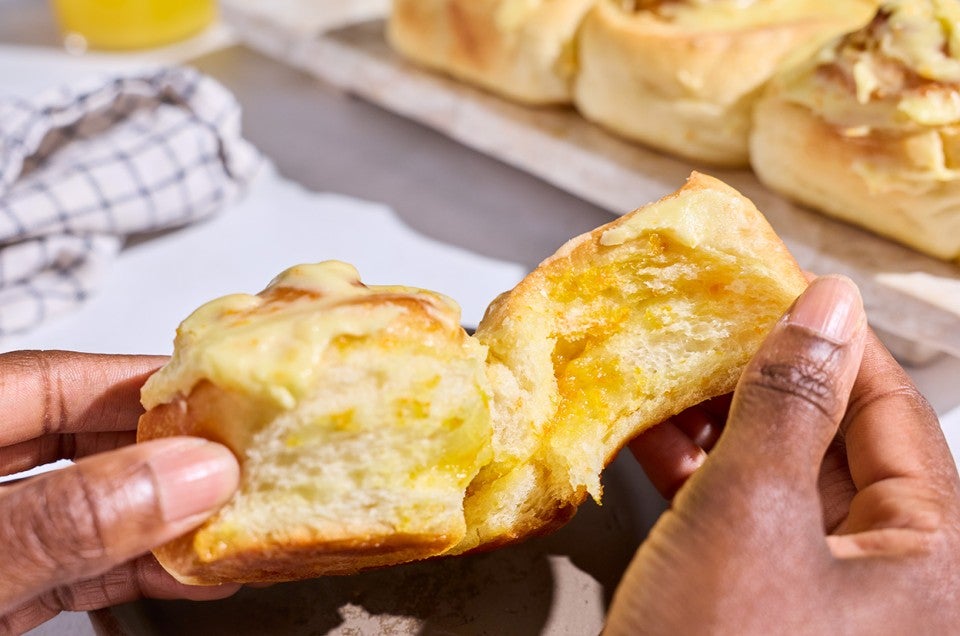 Pulling apart a Fluffy Frosted Orange Roll to show the light milk bread interior. - select to zoom