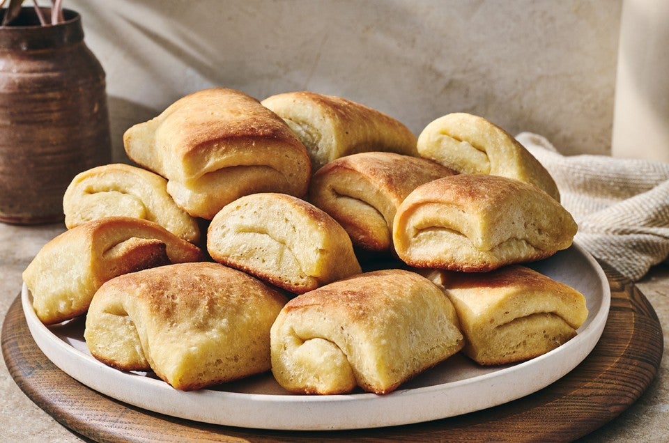 A plate loaded up with Parker House rolls showing their golden exterior and classic fold. - select to zoom