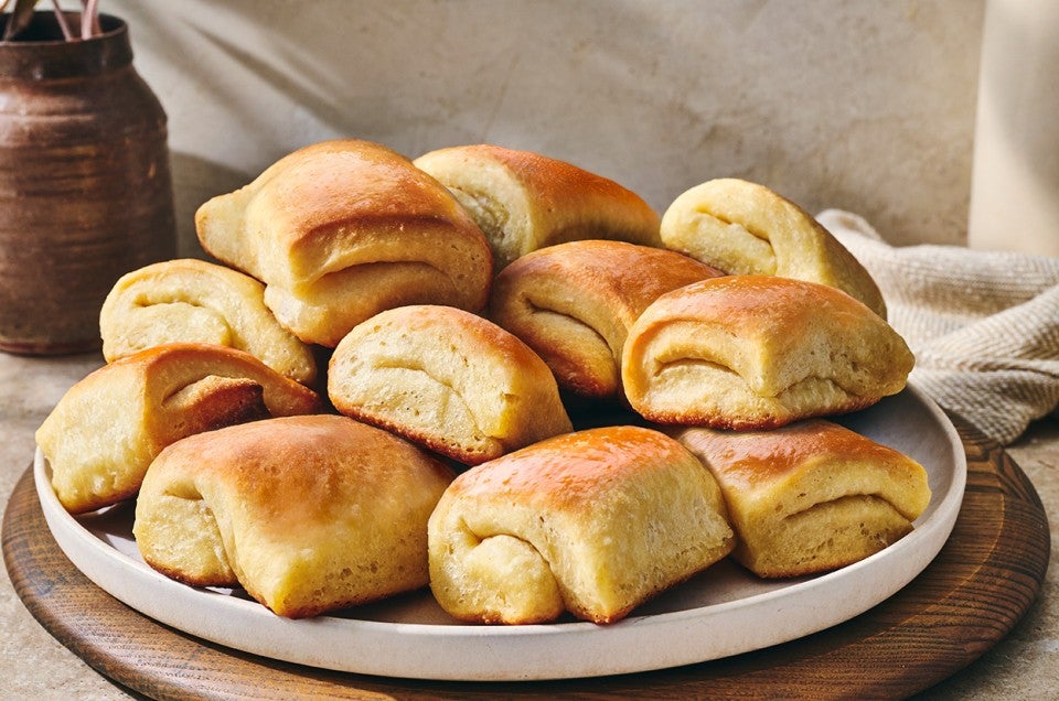Parker house rolls stacked on a plate showing a buttery gloss and perfect folded bake. - select to zoom