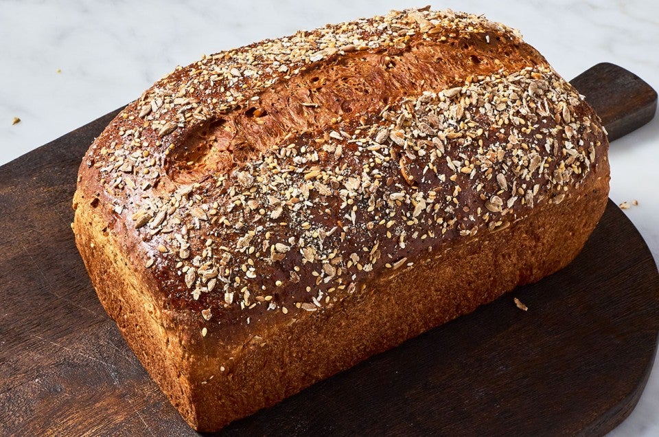 A loaf of Multigrain Protein Bread on a dark brown cutting board. - select to zoom