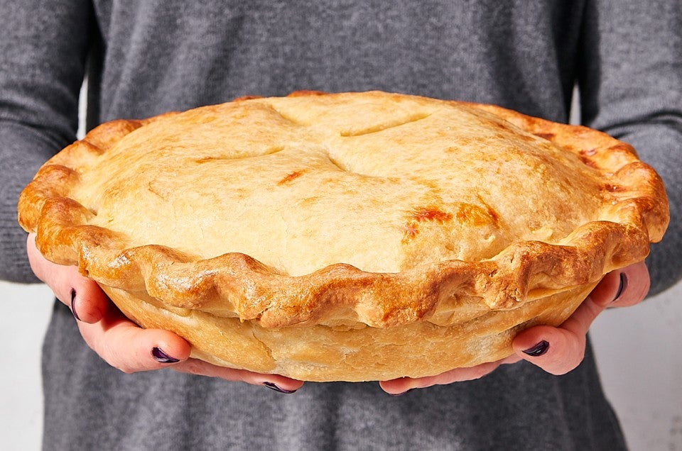 A person with a grey dress holding a large, perfectly golden, baked thanksgiving leftover pie. - select to zoom