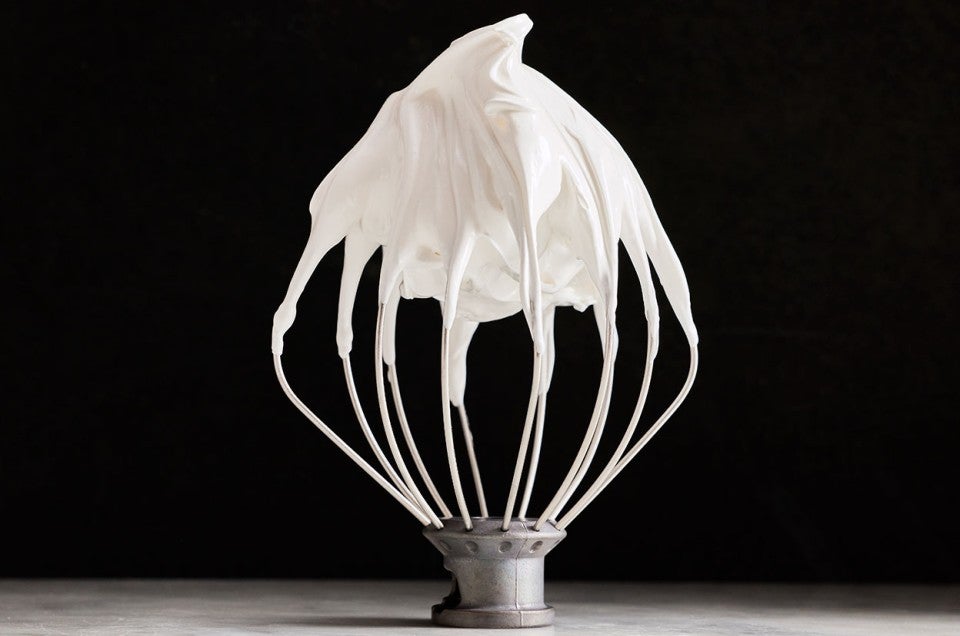 White Swiss Meringue on a mixer whisk shown upright against a black background. - select to zoom