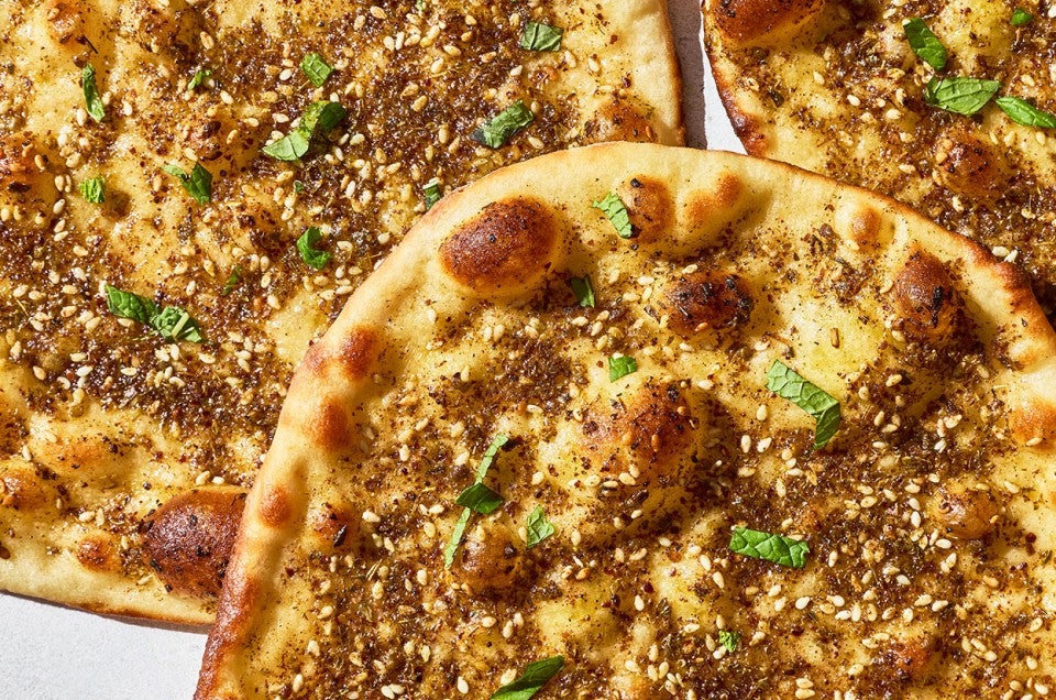 Za’atar Manakeesh seen from above with toppings, browned bubbly flatbread, and arranged atop each other. - select to zoom