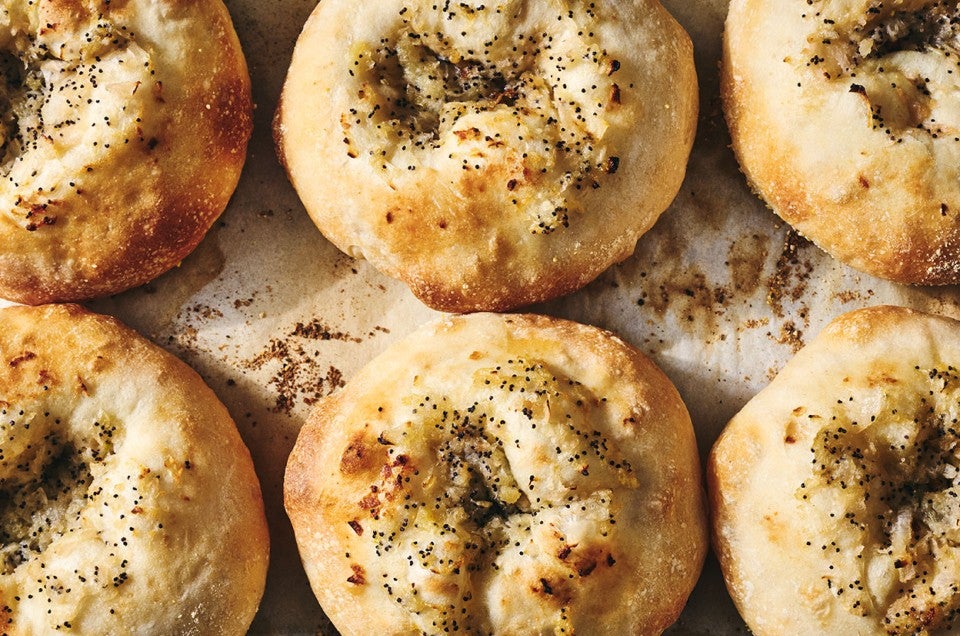 Classic Bialys on a sheet tray fresh out of the oven showing a beautiful crust and herbs on top of them. - select to zoom